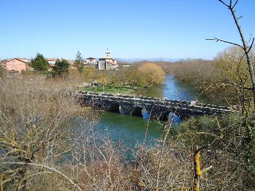 Steinbrücke über den Zadorra-Fluss, mit Kirche und Häusern im Hintergrund.