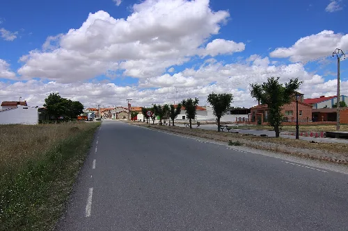 Straße in Cabizuela mit Bäumen und Häusern, bewölkter Himmel.