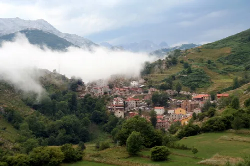 Vista de Tresviso con casas en las laderas y nubes en el cielo.