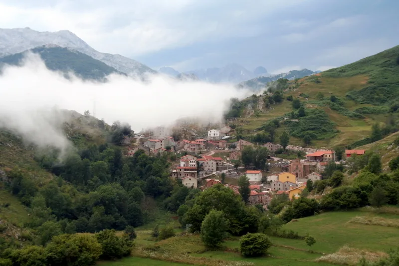 Vista de Tresviso con casas en las laderas y nubes en el cielo.