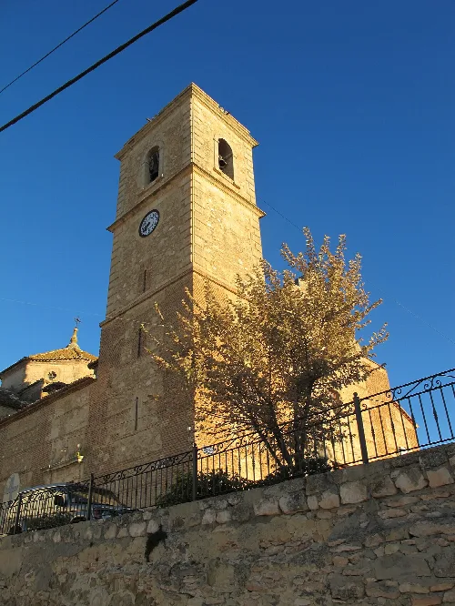 Torre de la iglesia de Alatoz con reloj y árbol en primer plano.