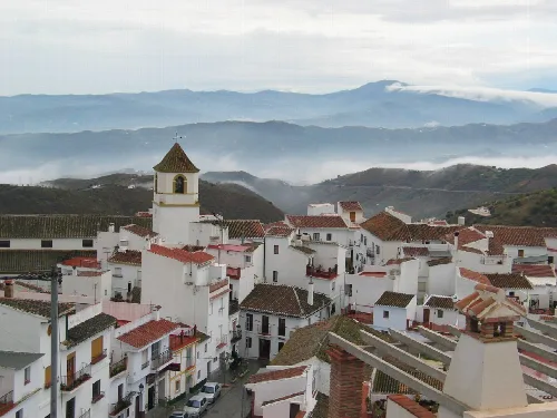 Weiße Häuser und eine Kirche in Canillas de Aceituno mit Bergen und Wolken.