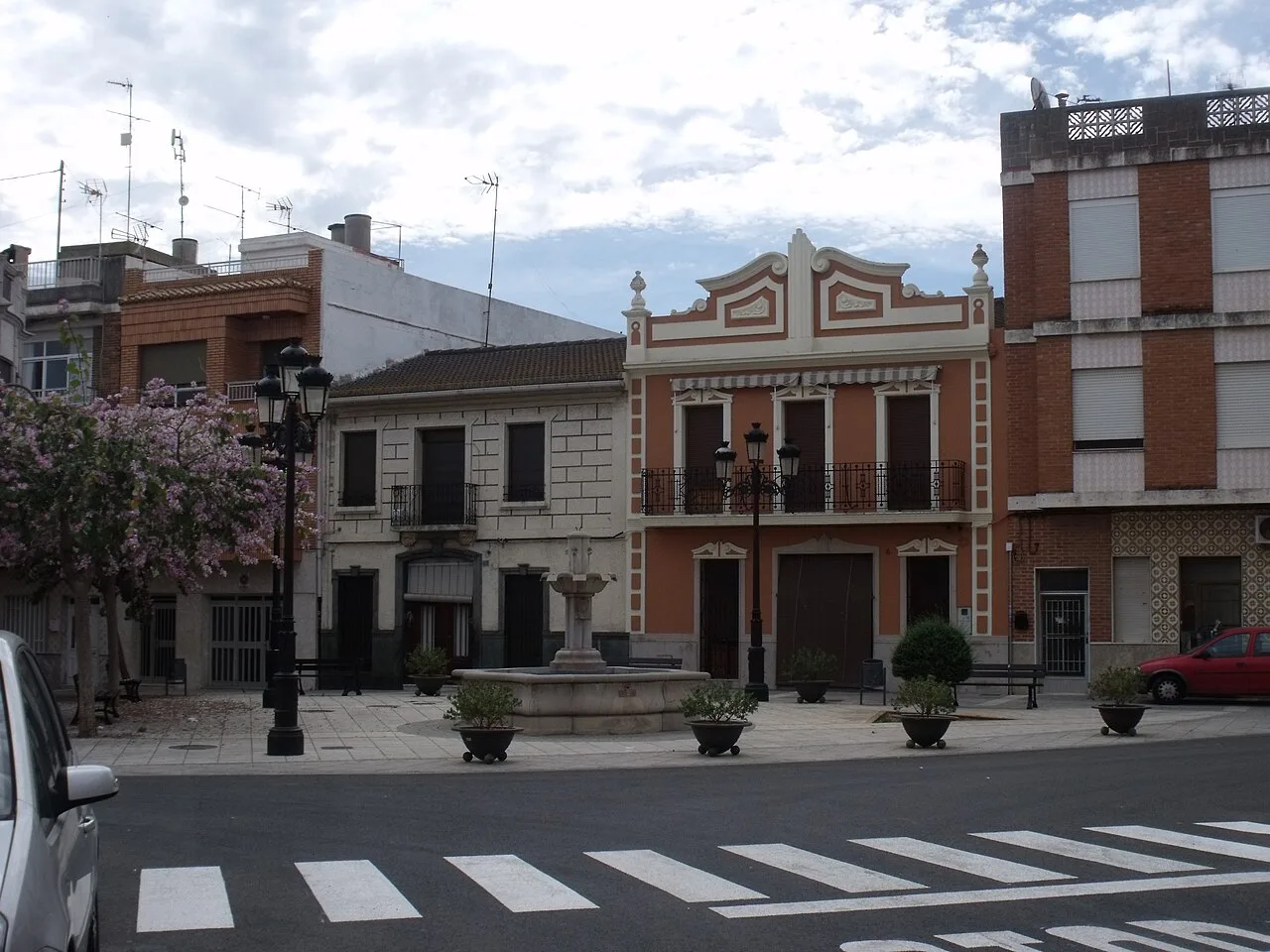 Plaza de la Iglesia en Llaurí con edificios y árbol en flor.