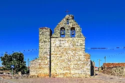 Fachada de una iglesia de piedra con campanario y cruz en la parte superior.