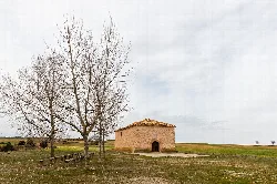 Small stone hermitage with trees and open field in Alconchel de Ariza.