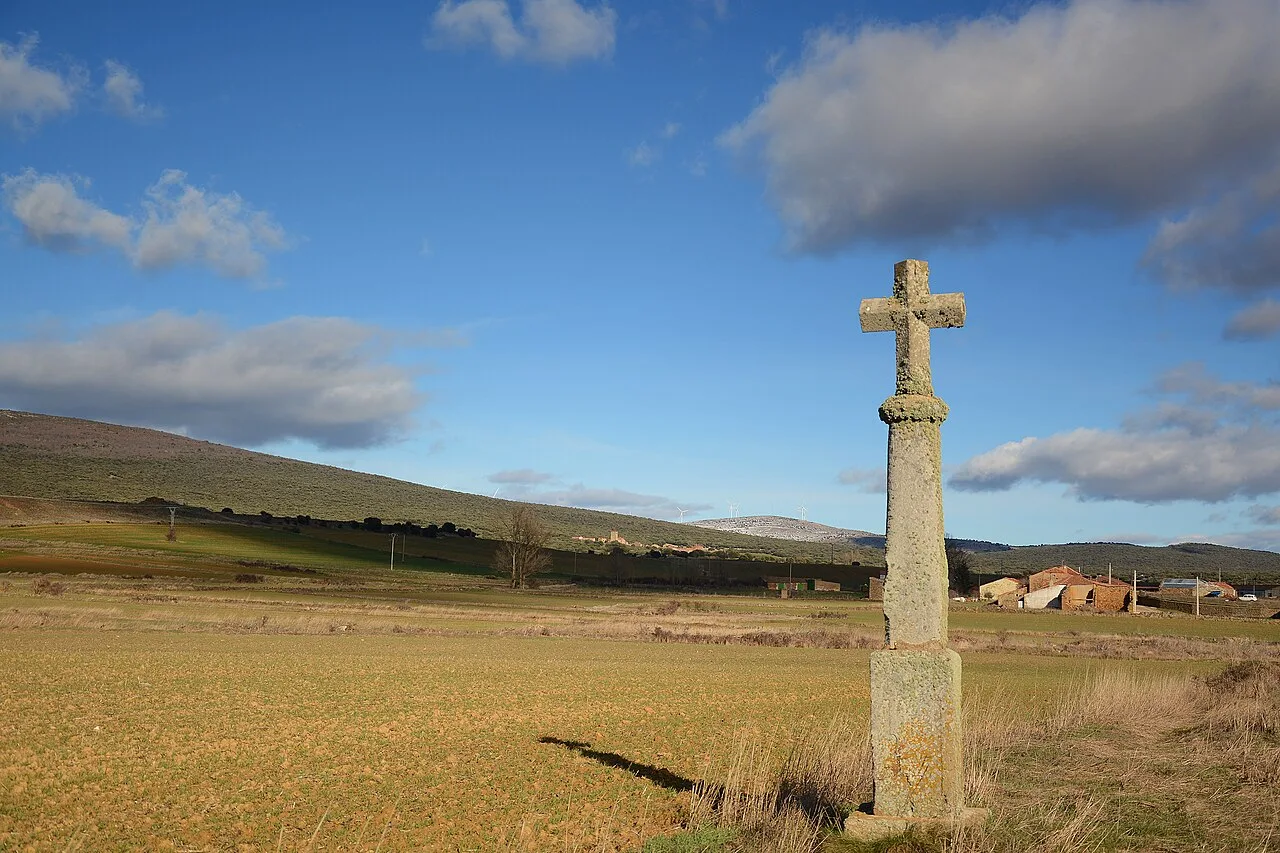 Cruce de piedra en un campo con colinas y cielo azul con nubes.