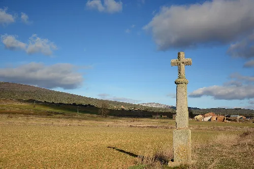 Steinkreuz in einem Feld mit Hügeln und blauem Himmel mit Wolken.