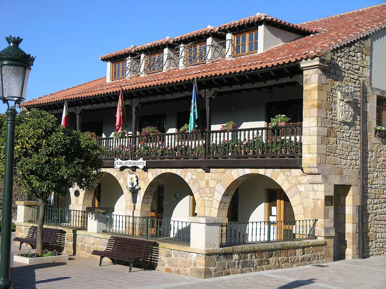 Edificio de piedra con balcón y banderas en Novales, Alfoz de Lloredo.