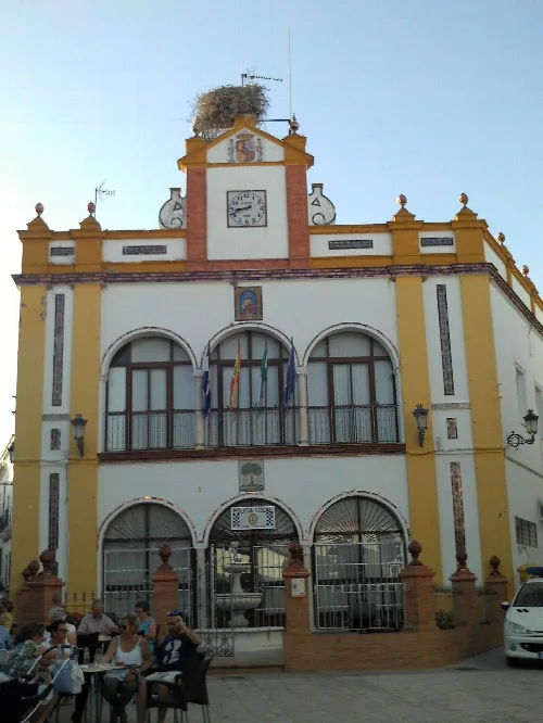 Town hall building with clock, flags, and a stork's nest on the roof.