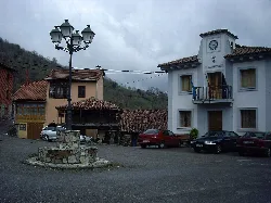 Square with clock tower, stone well, and parked cars in Villabre.