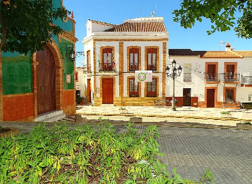 Vista de una plaza con edificios tradicionales y vegetación en Berrocal.