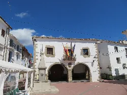 White building with arches at the entrance and flags on the facade in Pina de Montalgrao.