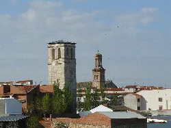 Two towers of different styles in the city center with rooftops and trees around.