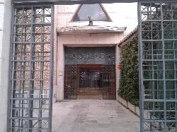Entrada con puertas de metal y vegetación a un lado en el Museo Municipal de Valdepeñas.