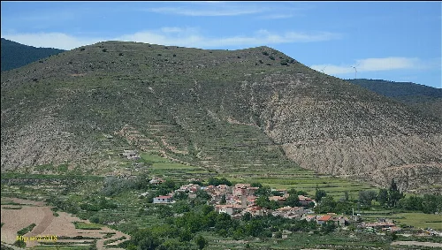 Kleines Dorf in einem Tal, umgeben von Hügeln mit Terrassenfeldern.