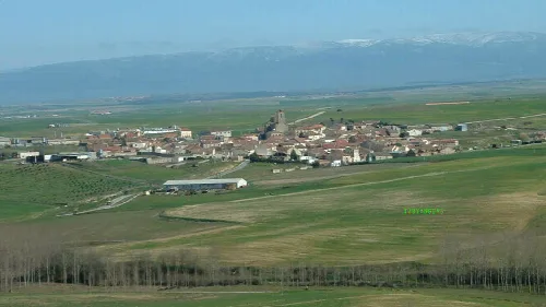 Panoramablick auf eine Stadt mit grünen Feldern und Bergen im Hintergrund.