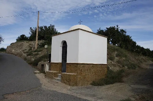 Capilla pequeña con paredes blancas, puerta negra y cúpula en Bentarique.