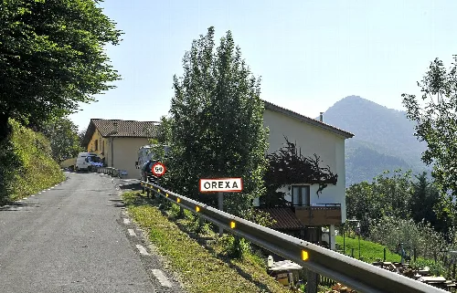 Eingang zum Dorf Orexa mit Schild und Häusern auf der Straße.