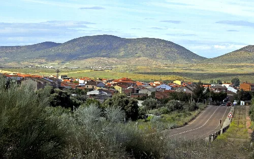 Dorf mit Häusern und Bergen im Hintergrund, von der Straße aus gesehen.