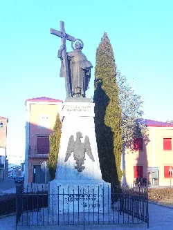 Estatua de San Juan de la Cruz con cruz y escudo en Fontiveros.
