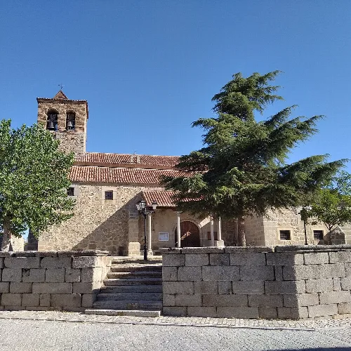Hof und Eingang einer Steinkirche mit einem großen Baum und einem Glockenturm