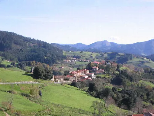Paisaje de colinas verdes con casas y montañas en la distancia.