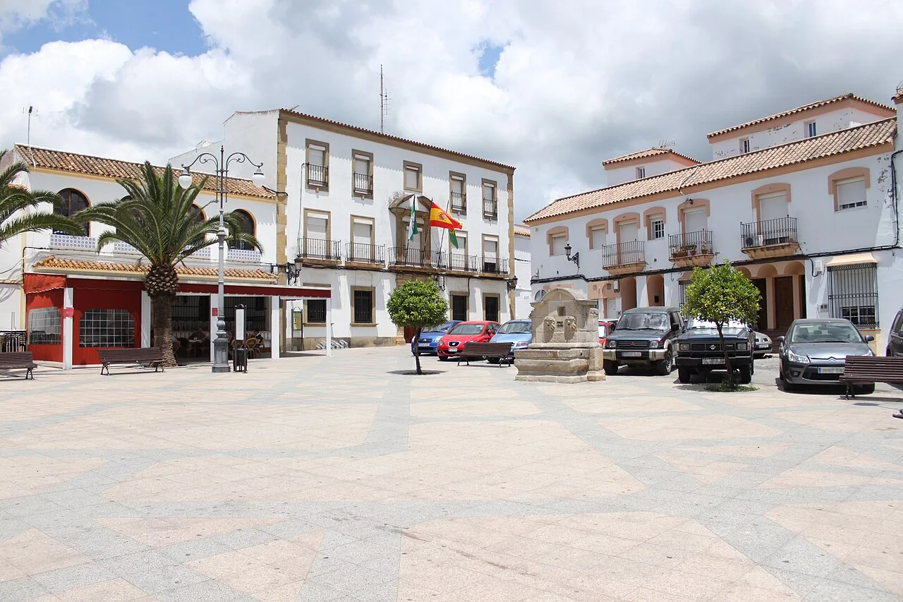 Square with palm trees, benches, and parked cars in Los Barrios, Cádiz.