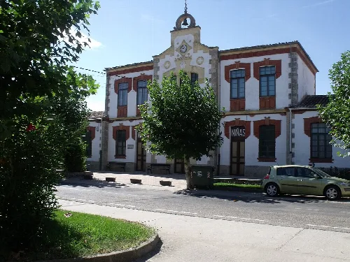 Klassisches Gebäude in Pozoantiguo mit weißer Fassade, roten Details und Bäumen davor.