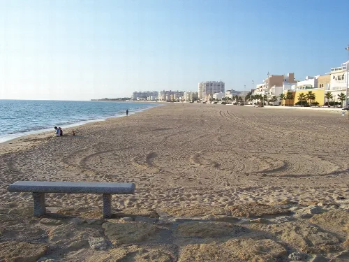 Sandstrand mit Gebäuden und Palmen in Rota, Cádiz.