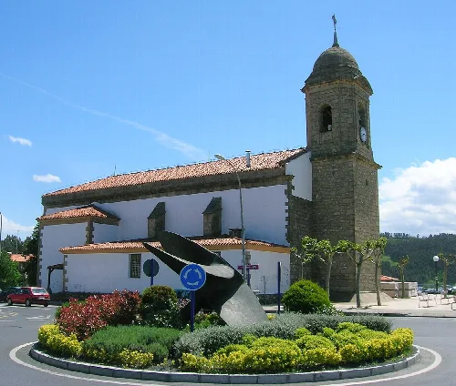 Iglesia de San Pedro en Sopelana con reloj y jardín con esculturas.