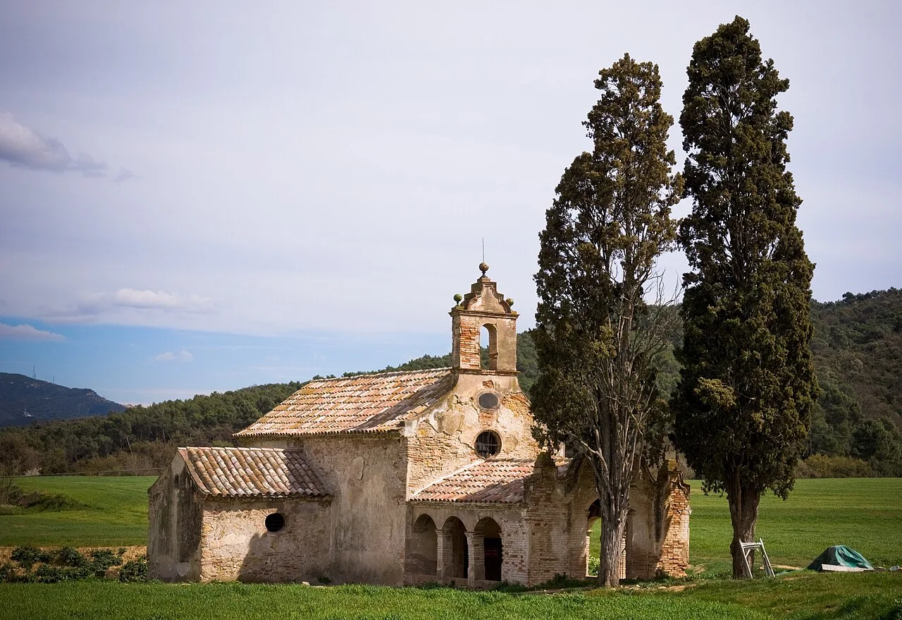 Kleine Kirche mit Glockenturm und zwei großen Bäumen im ländlichen Landschaft.