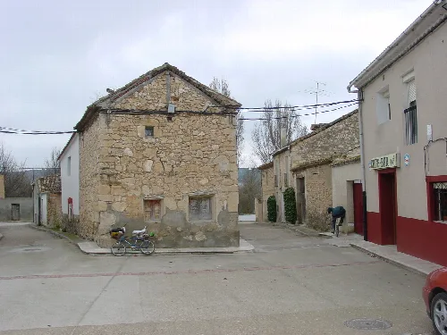 Casas antiguas y modernas en una calle de Valbuena de Duero, Valladolid, con un ciclista y un bar.