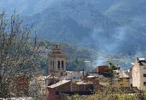 Blick auf ein Dorf mit Kirche und Häusern in einem Bergtal.