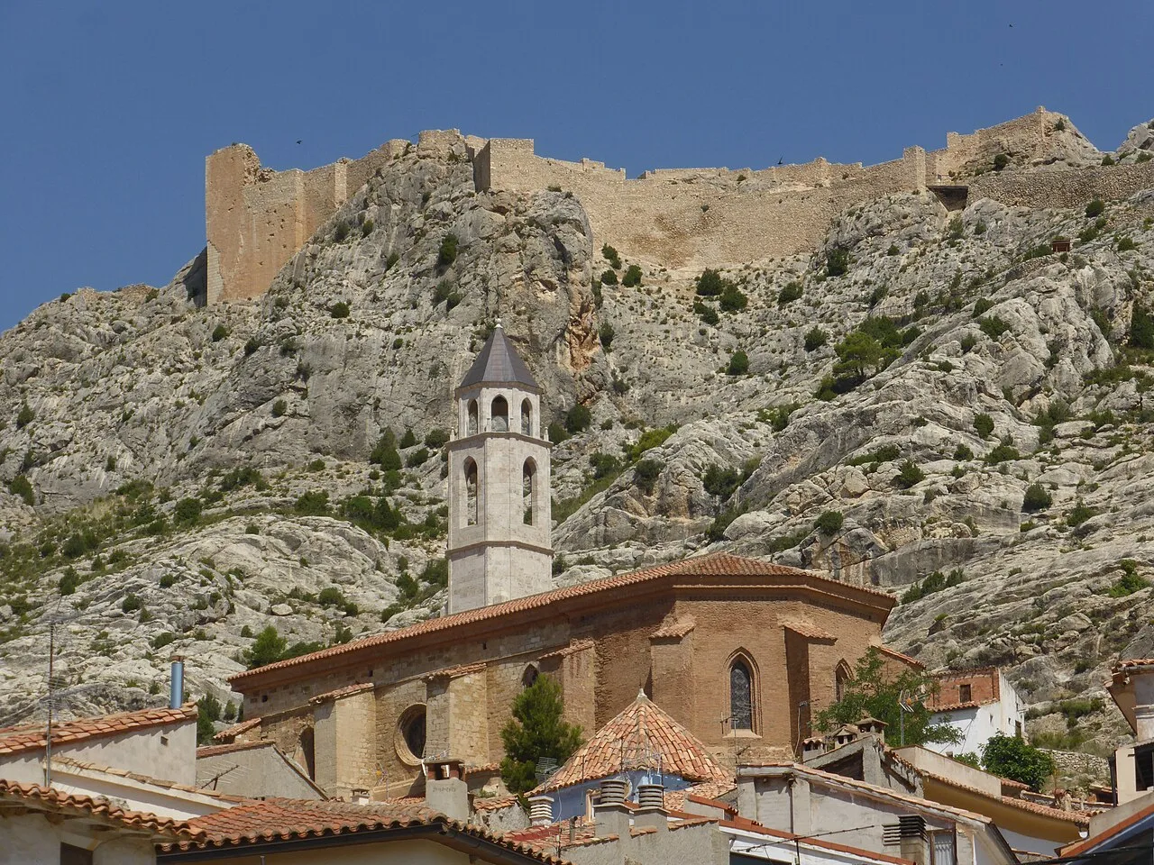 Iglesia de San Miguel con torre y castillo en lo alto de la colina.