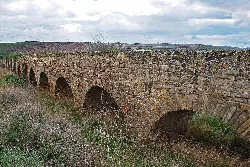 Acueducto romano de piedra con varios arcos en un paisaje rural.