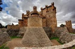 Castillo de Guadamur con muros altos y torres en un día nublado.