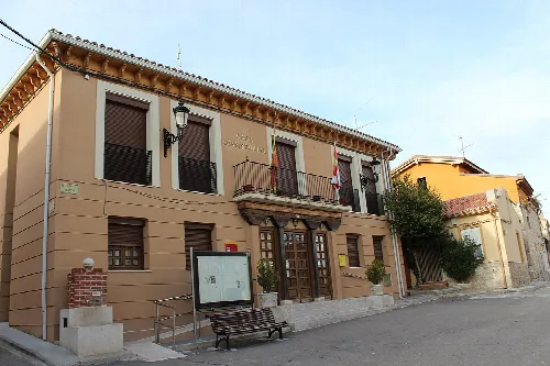Edificio del ayuntamiento con fachada beige y ventanas con persianas oscuras.