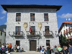 Stone building with windows and balconies, in a square with many people.