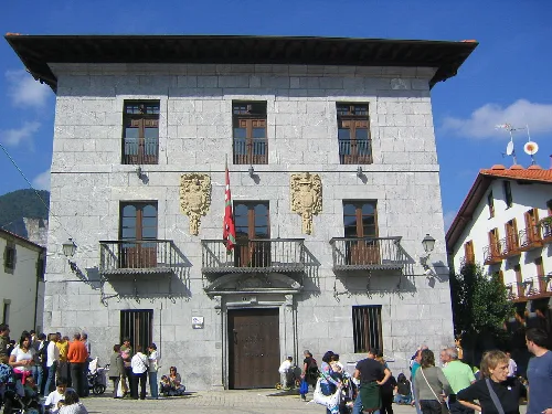 Edificio de piedra con ventanas y balcones, en una plaza con muchas personas.
