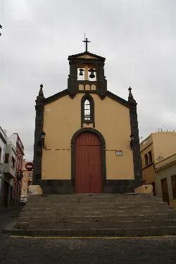 Fachada de una iglesia con escalones y campanario con cruz en la parte superior.