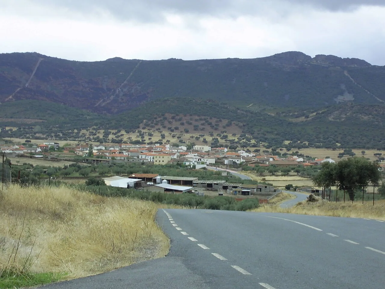 Straße, die zu einem Dorf mit Bergen im Hintergrund führt.