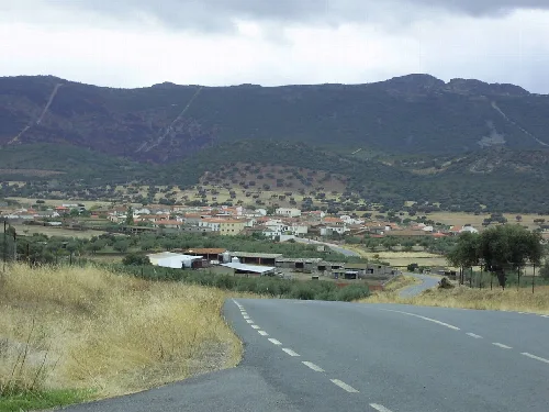 Straße, die zu einem Dorf mit Bergen im Hintergrund führt.