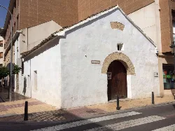 Pequeña capilla blanca con arco de ladrillo y puerta de madera en La Eliana.