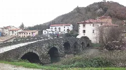 Puente de piedra sobre un río en Villava, Navarra, con casas y montañas.