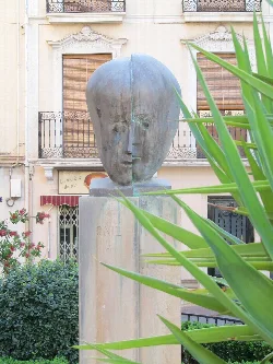 Escultura de una cabeza humana en un pedestal en un espacio urbano.
