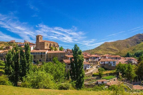 Paisaje de San Román de Cameros con iglesia y casas bajo un cielo azul.