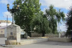 Steinbrunnen mit Wasserbecken und Waschplatz in Vellisca, Cuenca, umgeben von Bäumen und einer alten Straßenlampe.