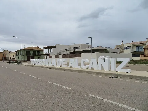 Große Buchstaben, die 'TORRECILLA DE ALCAÑIZ' auf dem Bürgersteig neben der Straße schreiben.