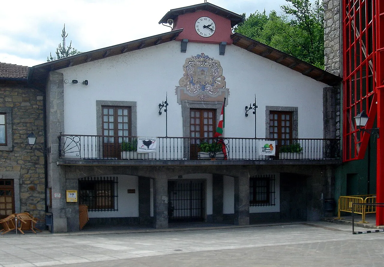 White building with clock and coat of arms, balcony and windows.