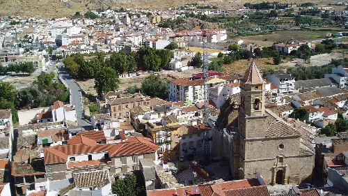 Blick auf eine Kirche im Vordergrund und Häuser in Loja, Granada, an einem sonnigen Tag.